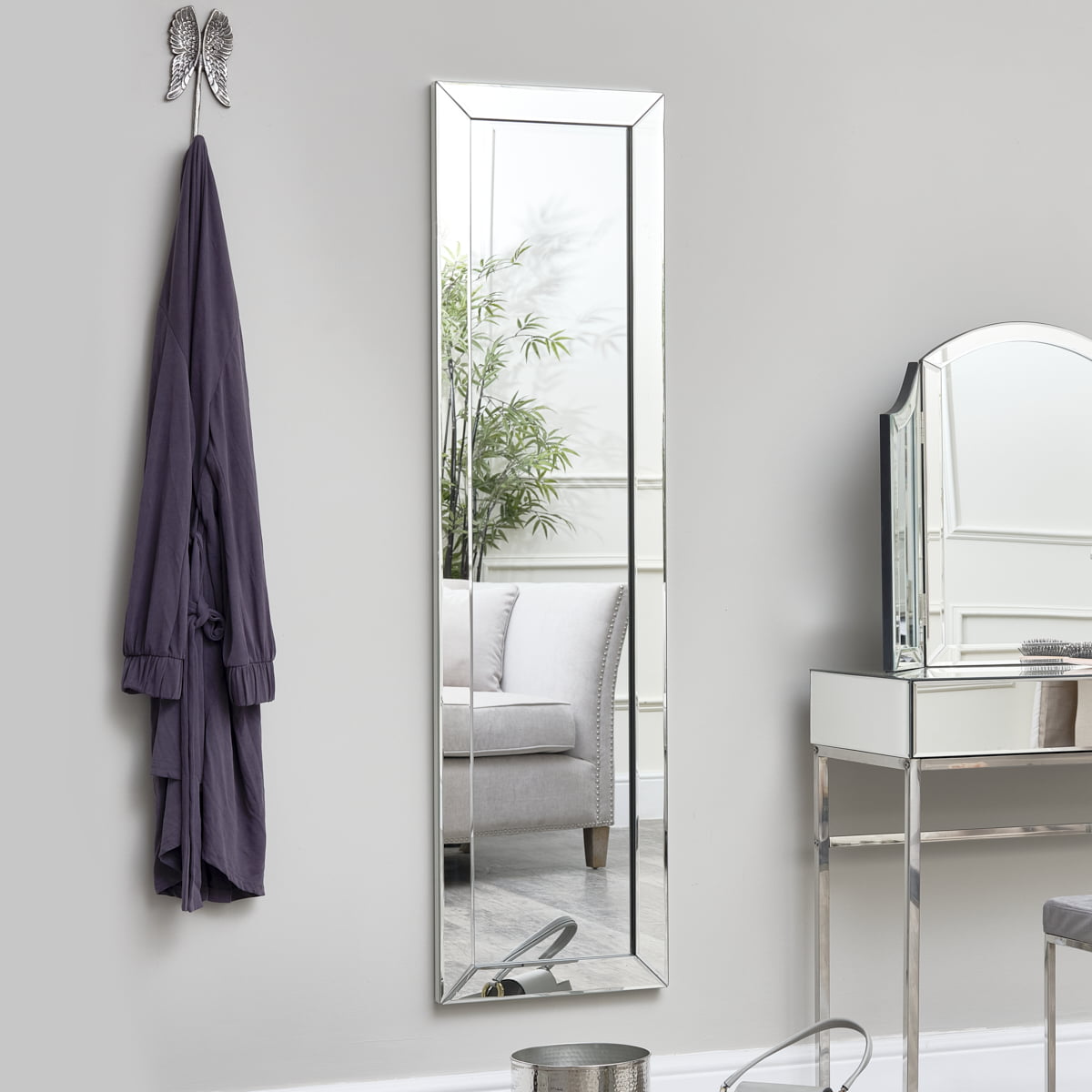 A full-length mirror in a modern room reflecting a cozy interior with a grey sofa and a potted plant