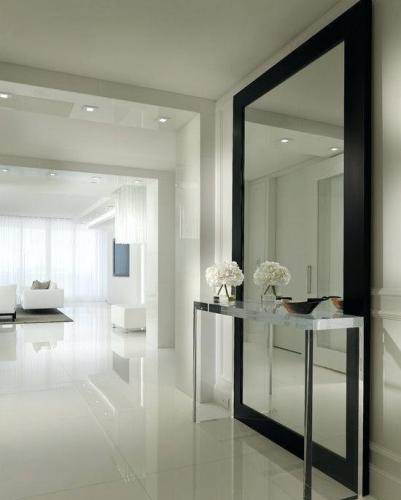 A sleek and modern interior with an expansive mirror reflecting a minimalist decor, featuring white walls, glossy floors, and refined accents creating an atmosphere of elegant simplicity.