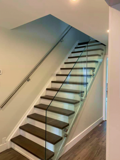 Modern staircase with custom glass side panels, wooden steps, and a metal handrail, located in a well-lit interior space.
