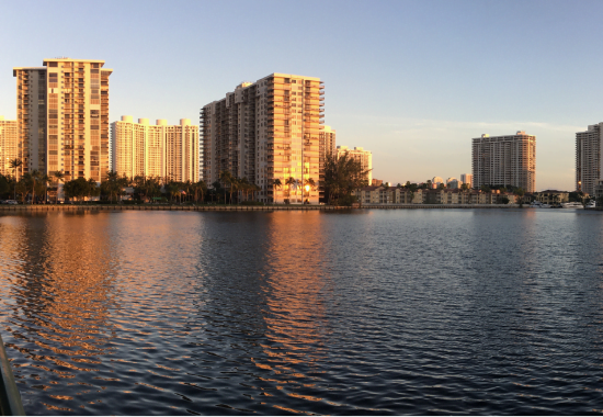 Sunset view over a calm river with reflections of high-rise buildings under a clear sky, featuring custom glass and mirrors.