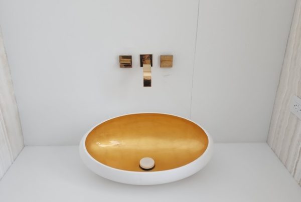 A sleek bathroom vanity with a white countertop featuring an elegant golden oval sink and modern gold fixtures against a white background.