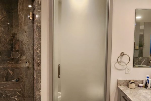 Modern bathroom with frosted glass partitions and marble finishes. The glass door leads to a shower area with marble detailing, next to a sink and mirror.