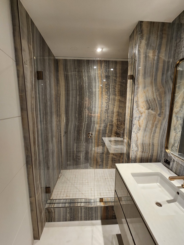 Modern shower cabin with transparent shower doors and walls, elegantly lined with marble featuring exquisite streaks of gray, brown, and gold hues.