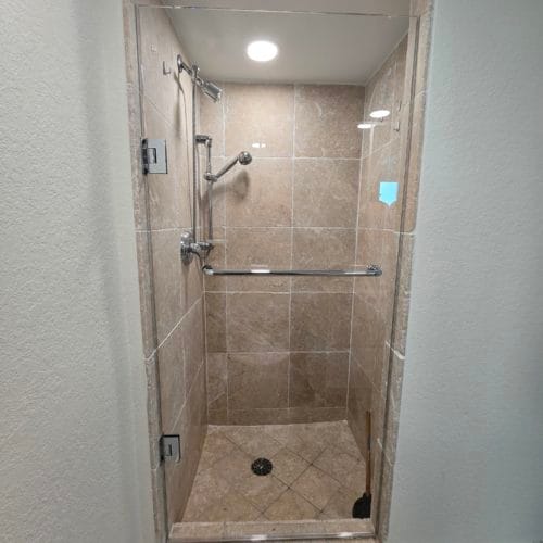 Clear glass shower door in a compact bathroom with beige tiles.