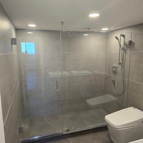 Spacious shower cabin with clear glass doors and grey tiles.