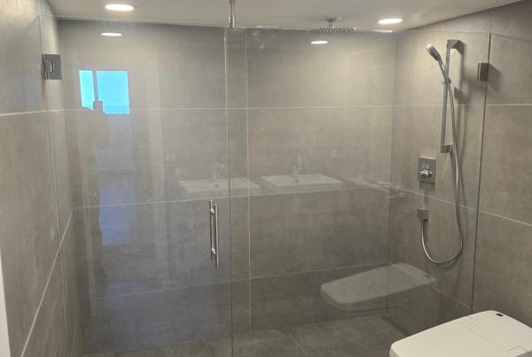 Spacious shower cabin with clear glass doors and grey tiles.